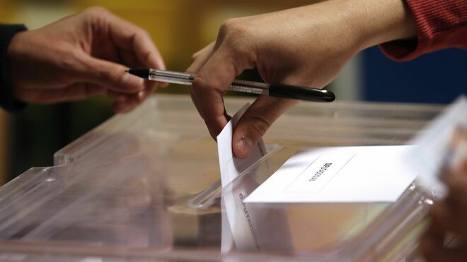 un elector introduce su voto en la urna en un colegio.
