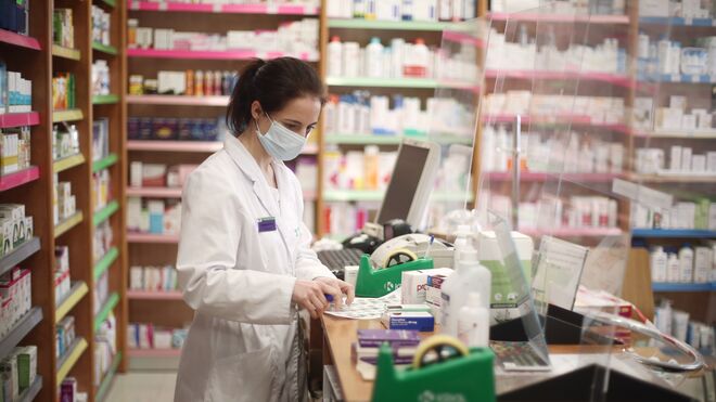 Una farmacéutica con mascarilla atiende a los clientes en una farmacia.