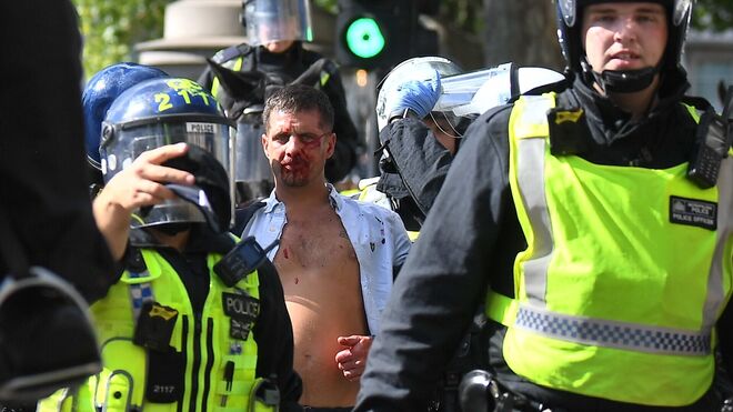 Un hombre herido es acompañado por agentes antidisturbios en Londres.