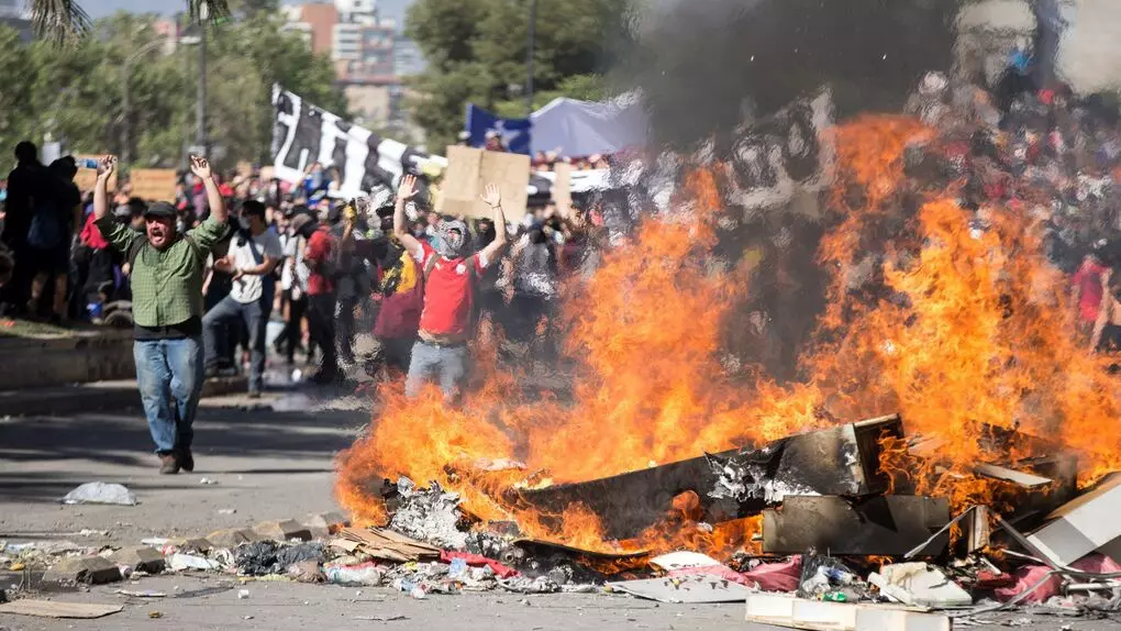 Manifestantes gritan arengas tras una barricada en llamas durante una jornada de protestas en Santiago (Chile)