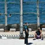 Un agente de Guardia Civil con un joven migrante marroquí en las inmediaciones de la valla de Ceuta, en la playa del Benzú