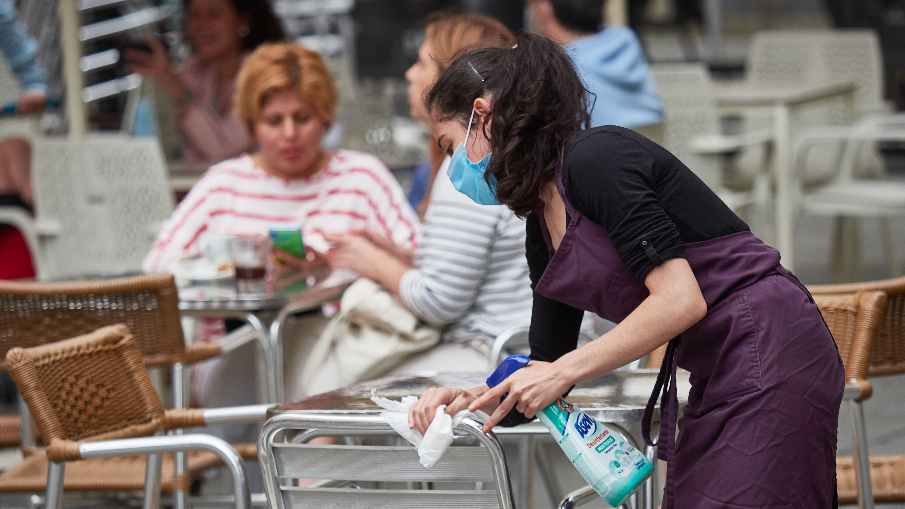 Una trabajadora desinfecta las mesas y sillas de una terraza de un bar.