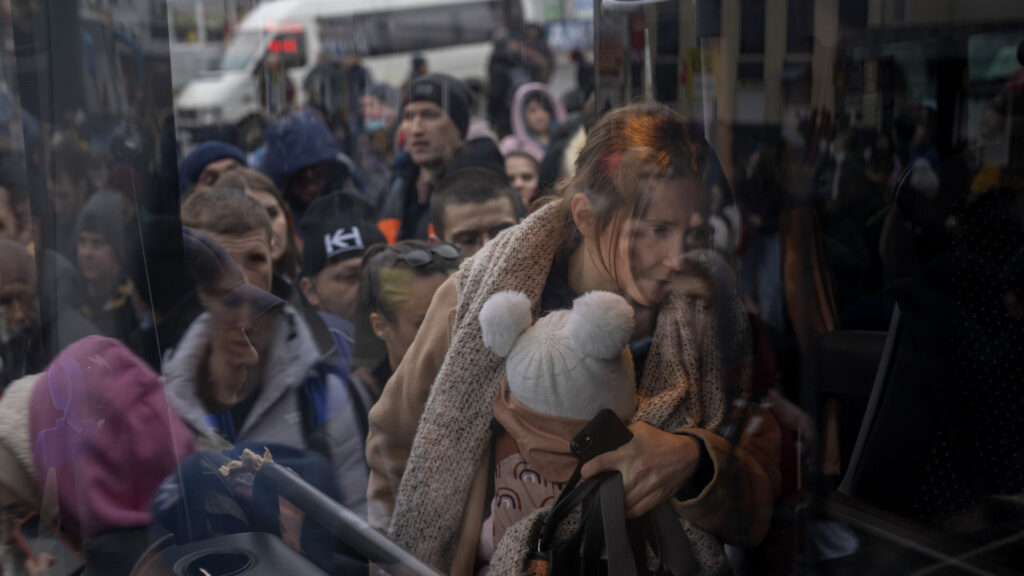 Una mujer sostiene a su bebé antes de entrar en un autobús para dejar Kiev (Ucrania)