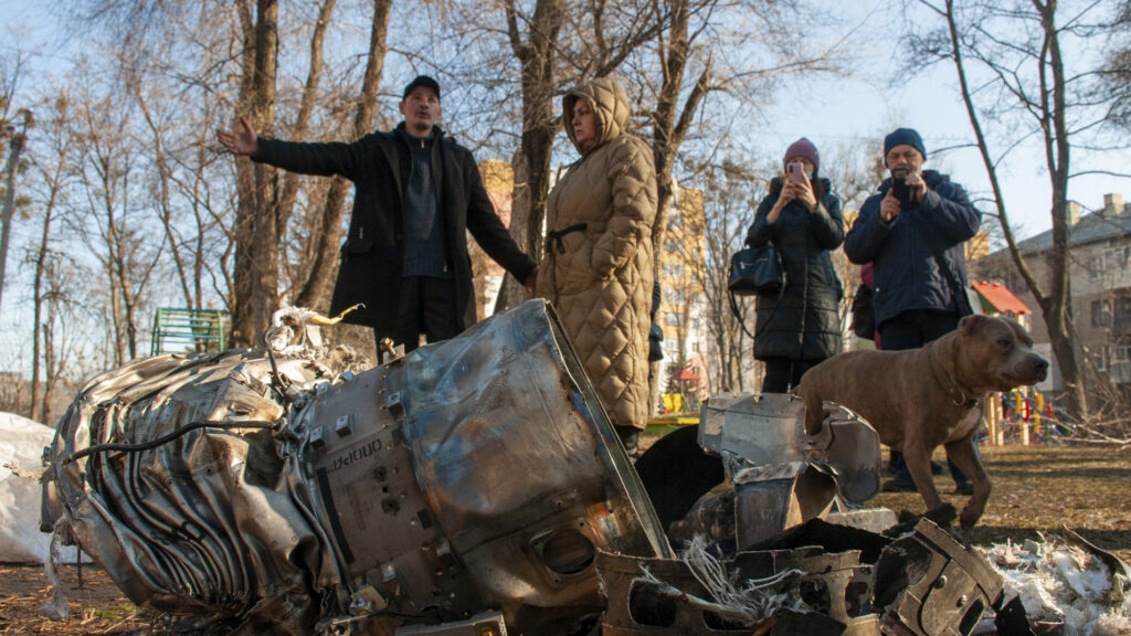 Personas en Ucrania junto a fragmentos de material militar tras el ataque de Rusia.
