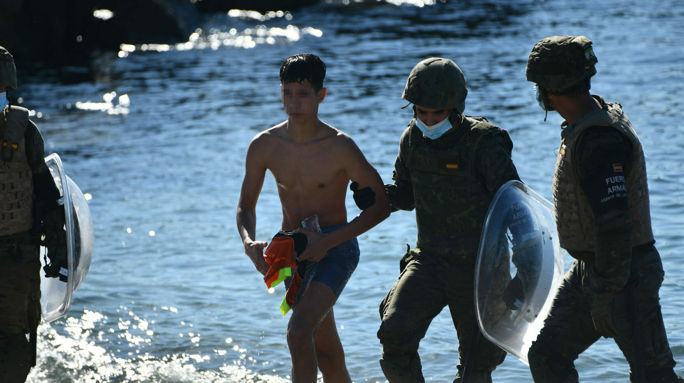 Dos militares del ejército español ayudan a un menor migrante procedente de Marruecos a su llegada a Ceuta