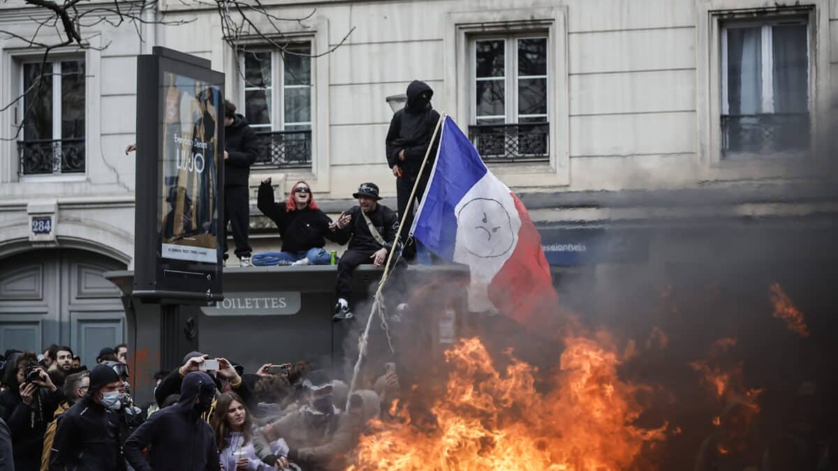 Unos manifestantes, con una bandera francesa, queman un montón de basura en París.