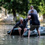 La gente ayuda a un anciano a subirse a un bote inflable mientras evacua de su casa en una calle inundada de Kherson
