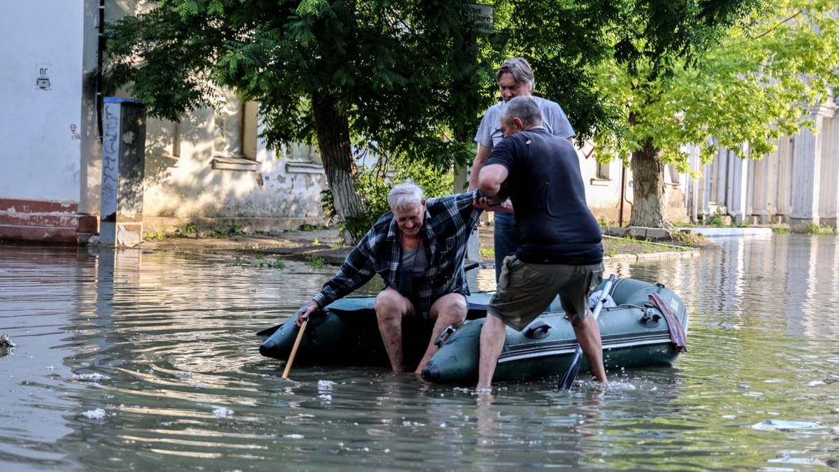 La gente ayuda a un anciano a subirse a un bote inflable mientras evacua de su casa en una calle inundada de Kherson