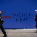 Policías antidisturbios frente a una pintada pidiendo "Justicia para Nahel" en París, Francia