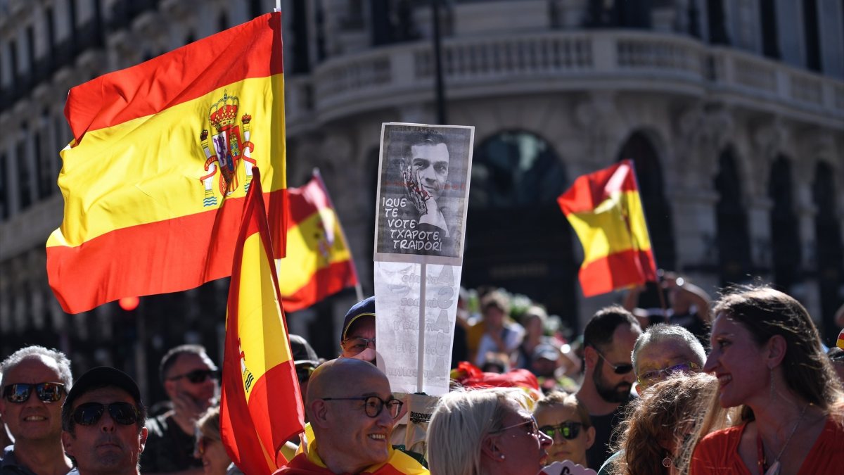 Personas con banderas de España y una pancarta con la imagen de Pedro Sánchez en la que se lee "Que te vote Txapote, traidor!"
