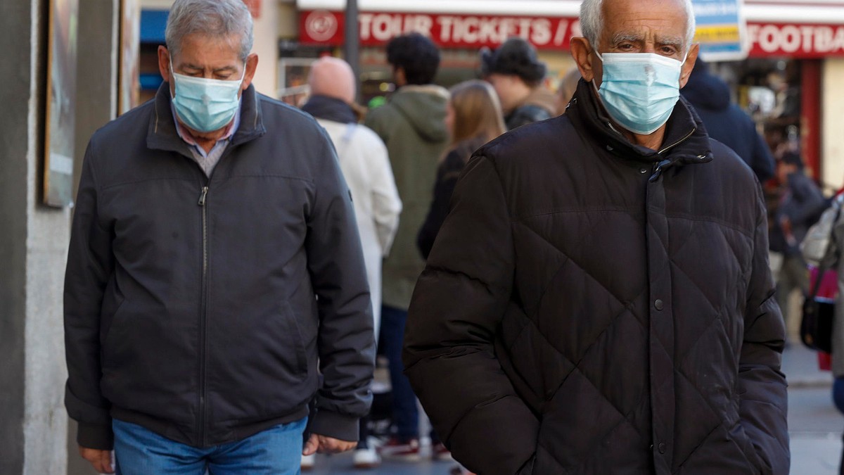 Dos hombres usan mascarilla mientras andan por la calle en Madrid