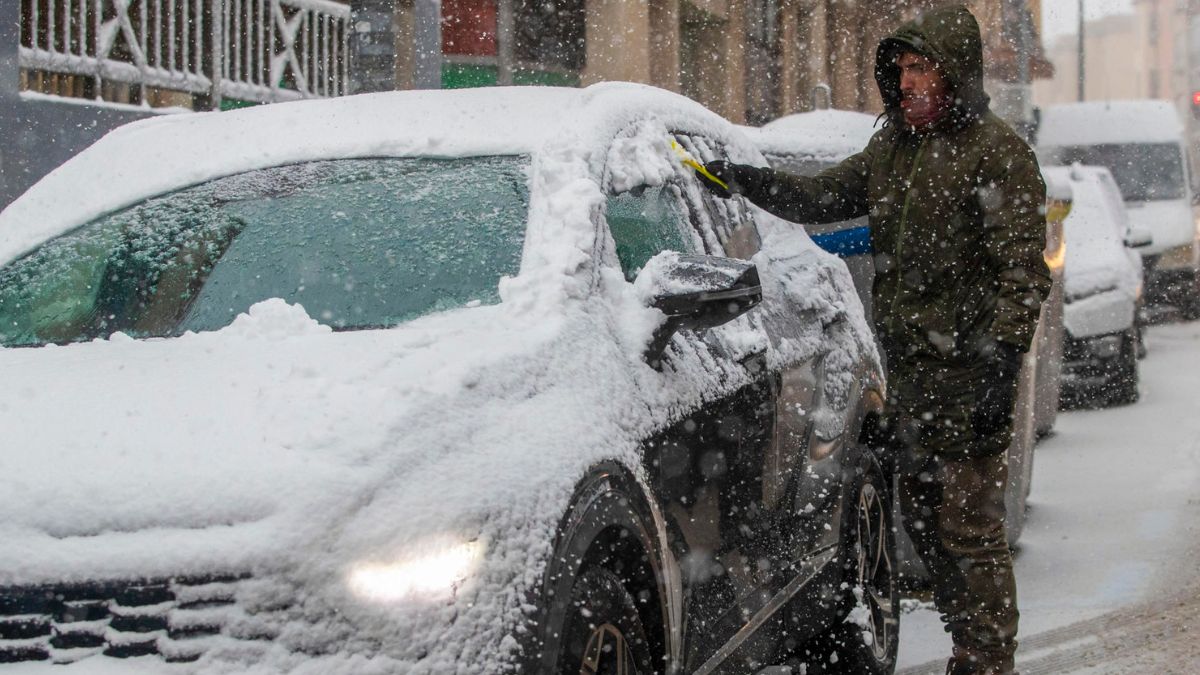 Un hombre retira la nieve de un vehículo durante la nevada de este viernes en Soria.