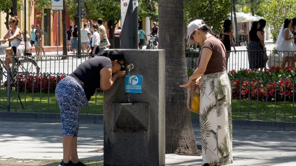 Una mujer se refresca en una fuente en Sevilla.